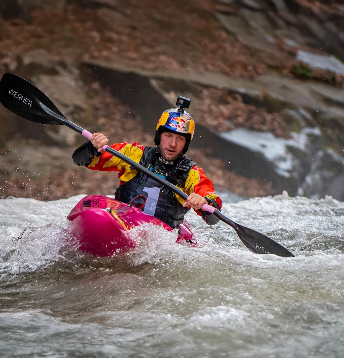 Whitewater kayaker in a pink kayak paddling through a rapid with a Werner paddle